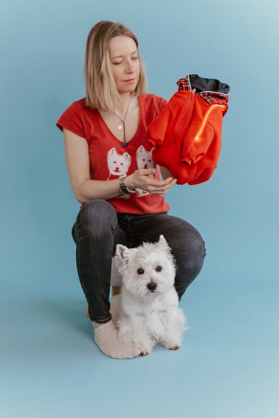 White dog westie sitting in fron givinbg high five dressed in red fleece hoodie with lighted reflects on arms