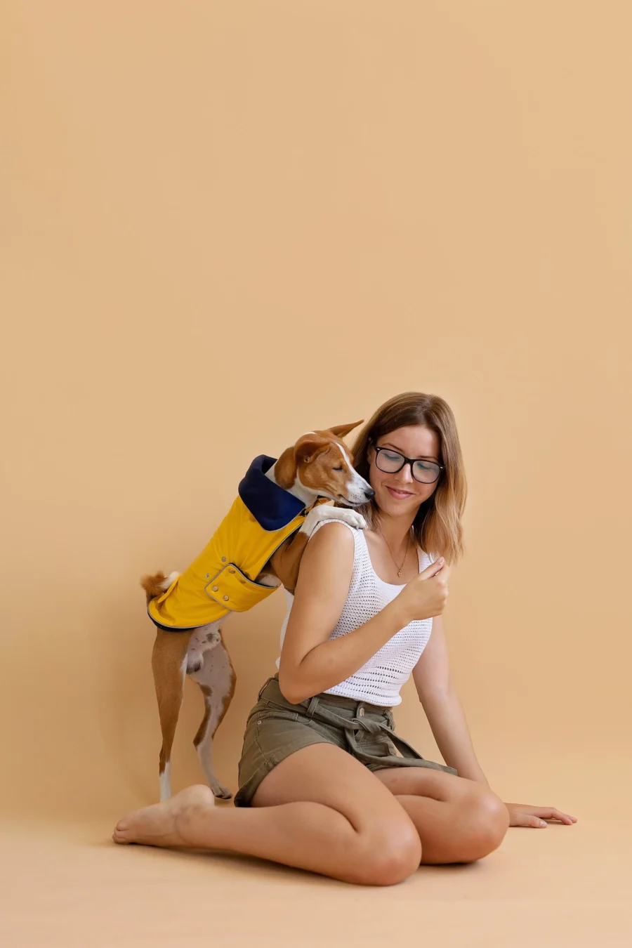 Basenji standing on two feet hugging his owner in beige background looking up and wearing yellow pvc dog coat in clasic yellow style. ciuciu. best dog raincoats